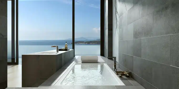 Contemporary bathroom featuring a built-in bathtub, grey stone wall and large floor-to-ceiling windows overlooking the sea.