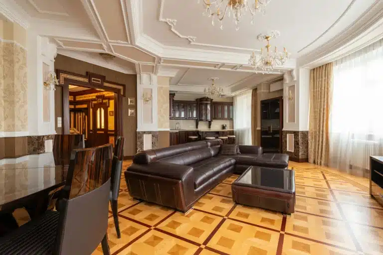 Grand classic living room with ornate coffered ceiling, crystal chandeliers, dark leather sofa and coloured marquetry parquet.